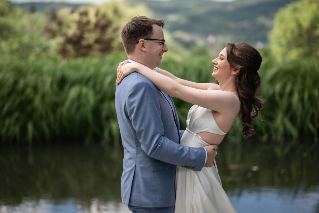 Braut und Bräutigam lachen beim Paarshooting am Wasser im Hofgut Hohenstein