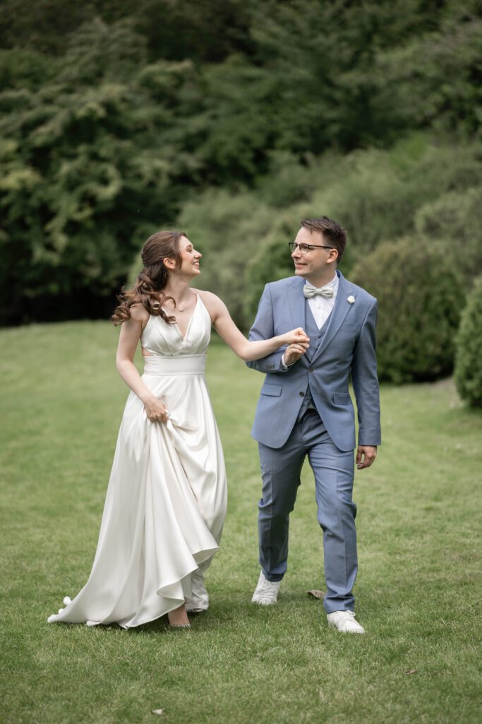 Braut und Bräutigam gehen Hand in Hand über eine Wiese im Hofgut Hohenstein