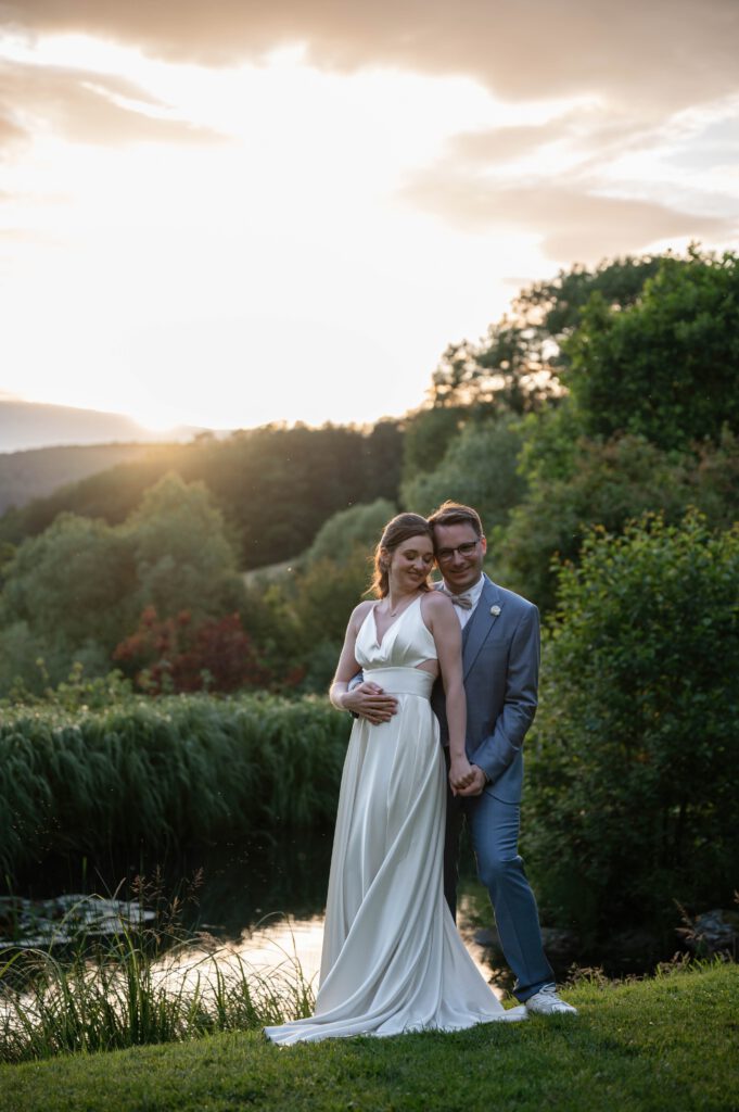 Braut und Bräutigam stehen am Wasser bei Sonnenuntergang im Hofgut Hohenstein