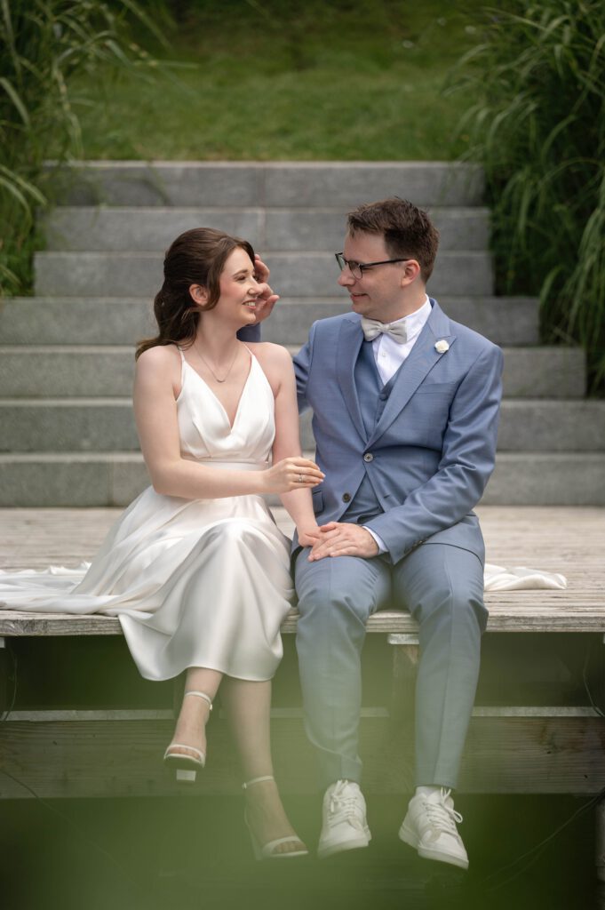 Braut und Bräutigam sitzen entspannt auf einer Holzbrücke im Hofgut Hohenstein