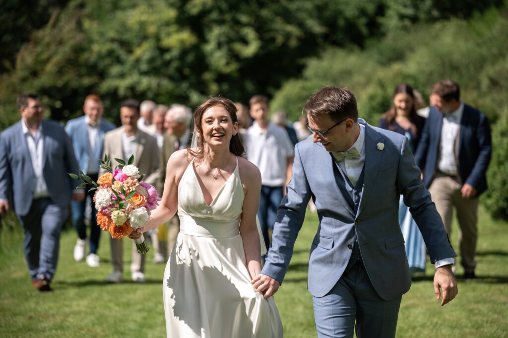 Brautpaar läuft nach der Trauung mit Gästen im Hintergrund im Hofgut Hohenstein