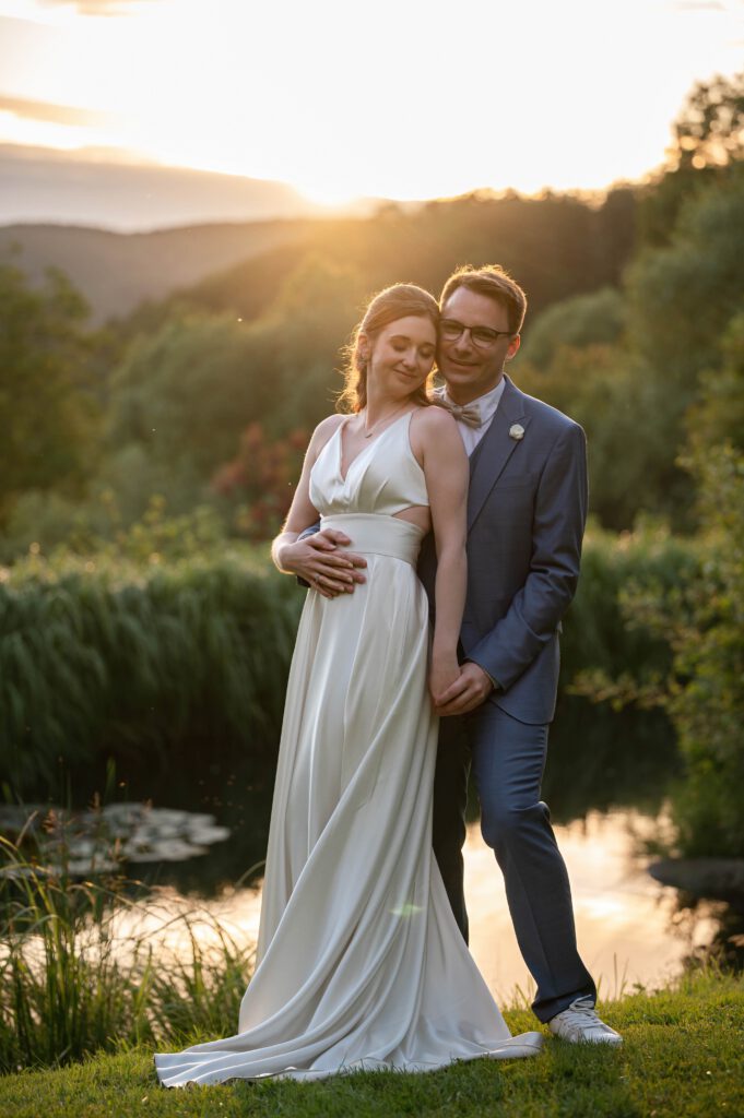 Brautpaar umarmt sich am Wasser bei Sonnenuntergang im Hofgut Hohenstein