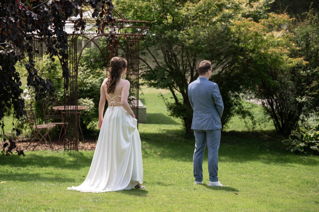 Braut nähert sich dem Bräutigam von hinten im Garten des Hofgut Hohenstein